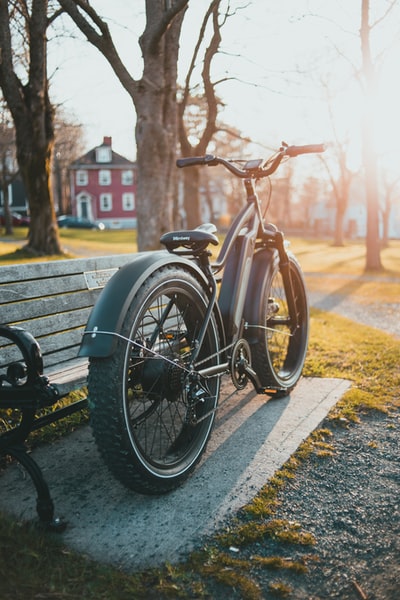 白天，黑色自行车停在棕色木长椅旁